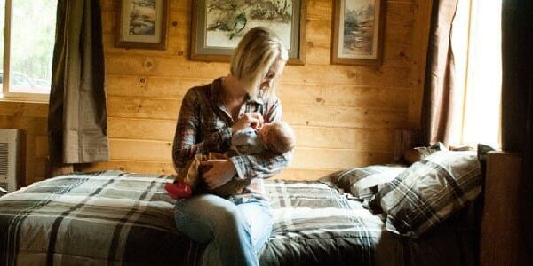 A woman sits on the bed in a cabin holding her baby