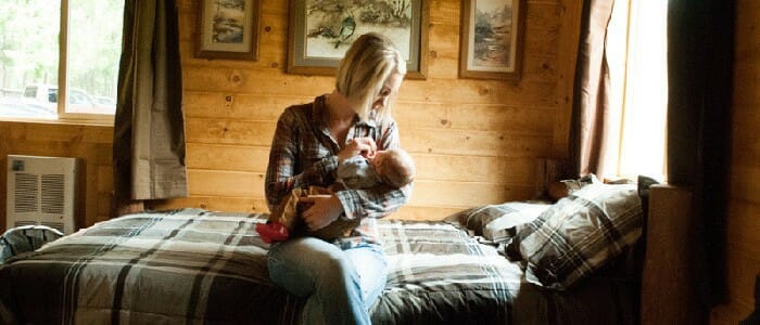 A woman sits on the bed in a cabin holding her baby
