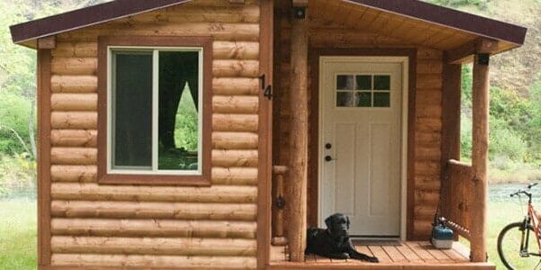 A dog sits on the porch of a cabin where two bikes are parked