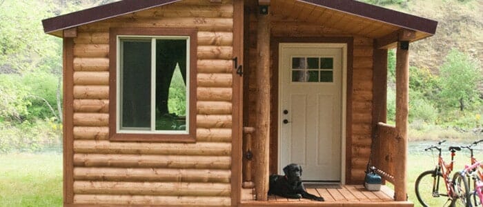 A dog sits on the porch of a cabin where two bikes are parked